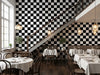 Papier peint damier noir et blanc posé dans un restaurant avec tables nappées de blanc et escalier