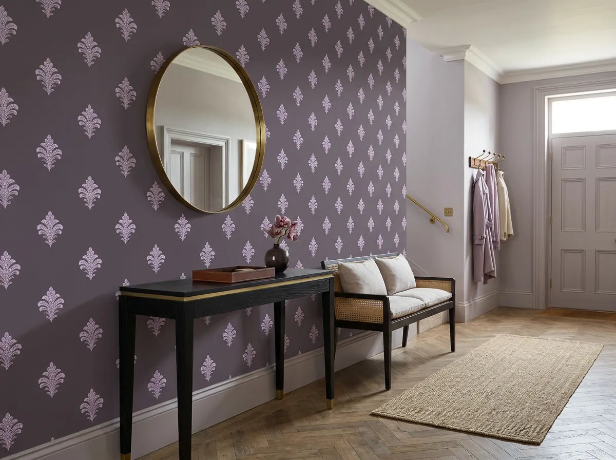 Papier peint fleurs de lys mauve sur fond gris posé dans une entrée avec console noire, miroir doré et banc