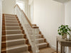 Papier peint beige jaune rayures posé dans l'escalier d'une maison avec tapis d'escalier et rampe blanche
