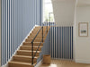 Papier peint rayures fines bleu marine posé dans une cage d'escalier moderne aux marches en chêne