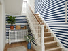 Papier peint rayures horizontales bleu marine posé dans l'escalier d'une maison avec rampe blanche