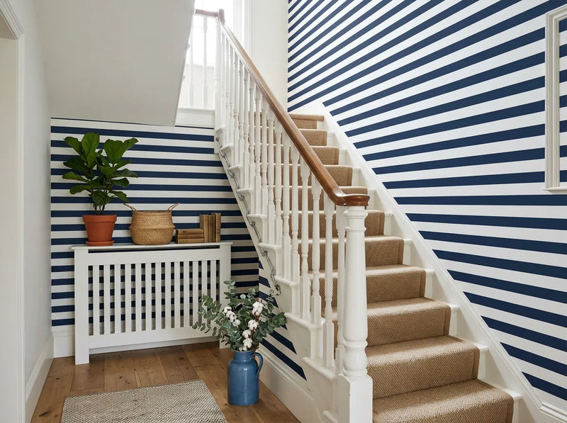 Papier peint rayures horizontales bleu marine posé dans l'escalier d'une maison avec rampe blanche