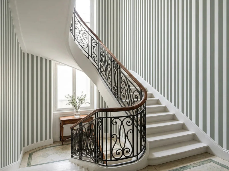 Papier peint rayures vertes posé dans une cage d'escalier tournante aux marches blanches et rampe en fer forgé